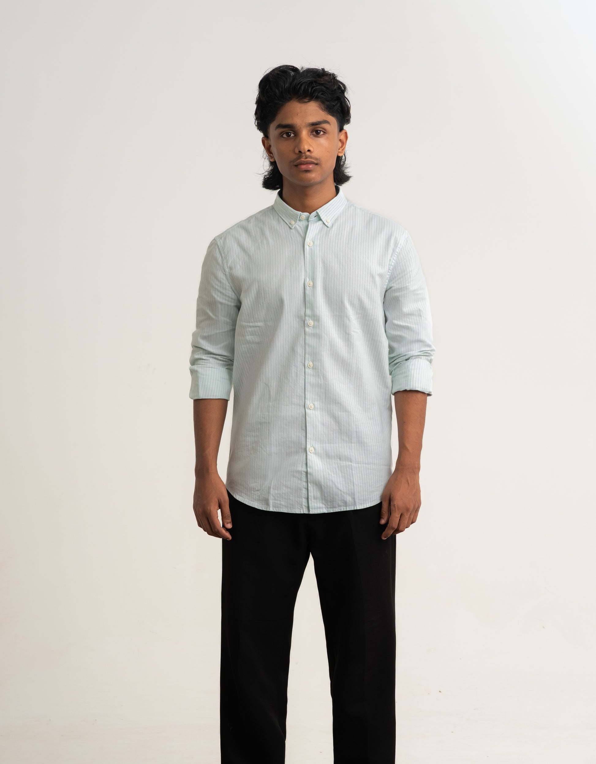 Person wearing a light-colored shirt and dark pants against a plain background