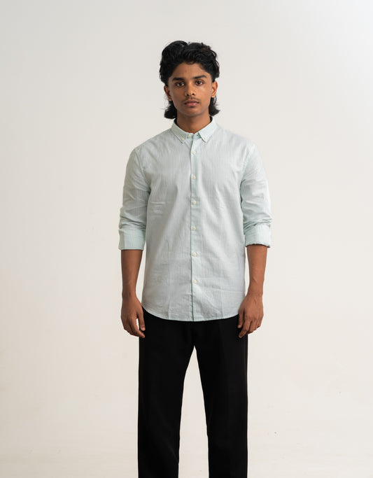 Person wearing a light-colored shirt and dark pants against a plain background